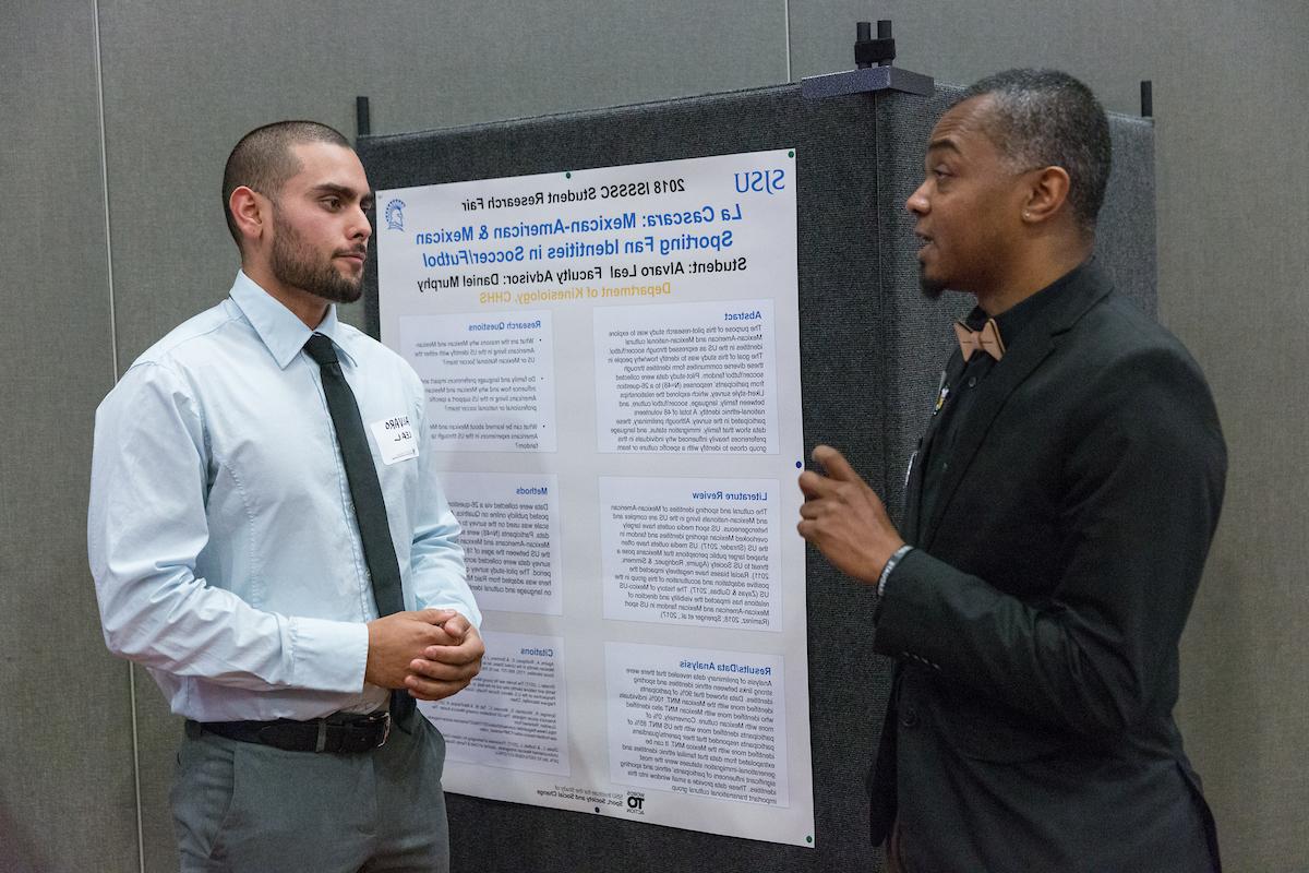 Two students talk in front of a research poster.