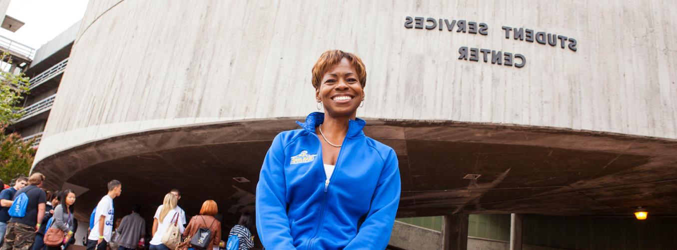 A smiling staff member standing in front of the student services center.