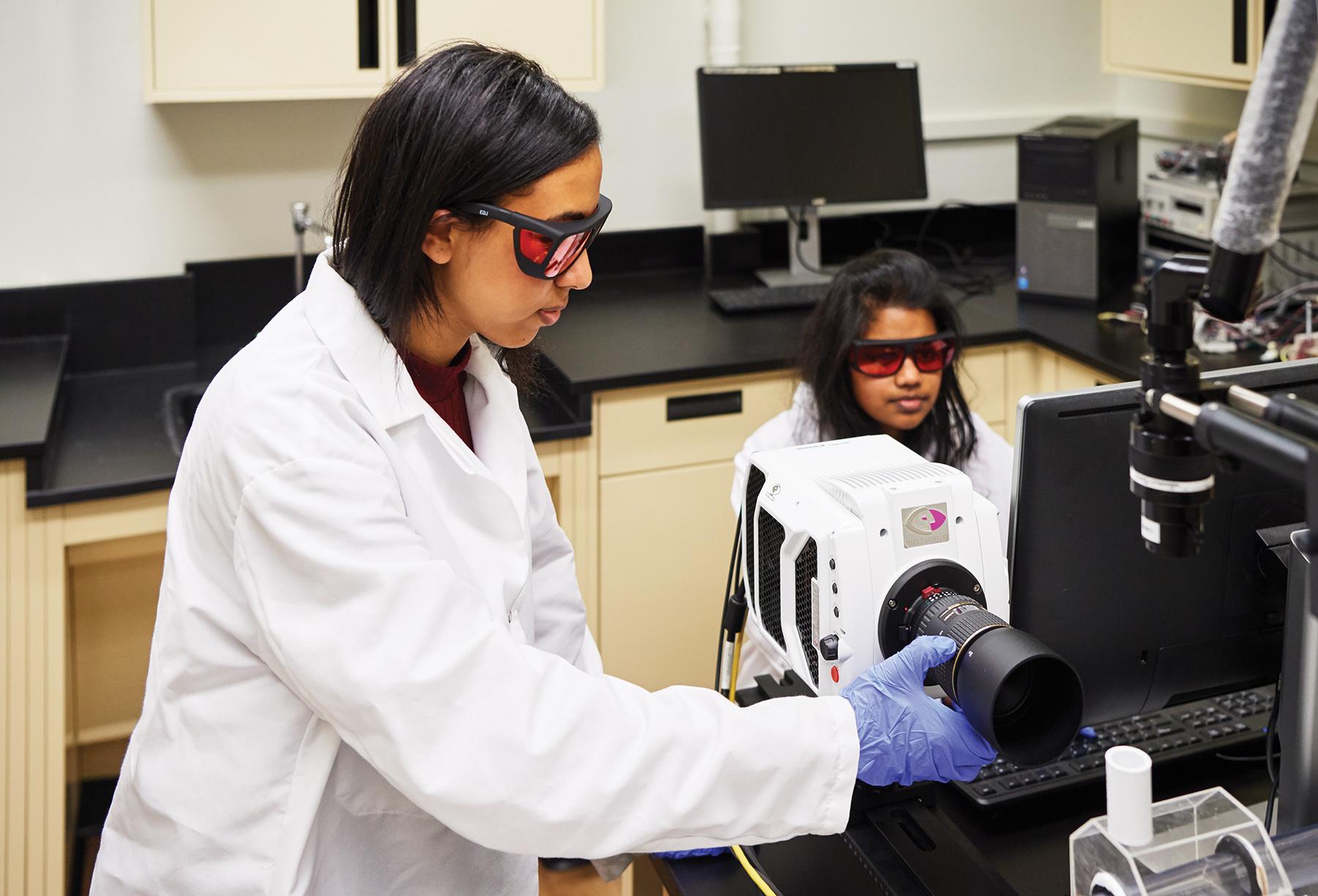 two female students in lab coats and goggles